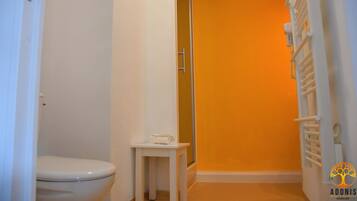 Un baño con inodoro, una mesita con una toalla y zona de ducha.