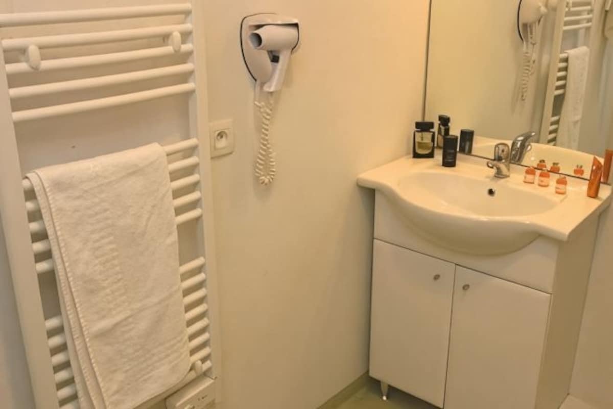 Un baño con lavamanos blanco, un espejo, un secador de pelo y un perchero para toallas.