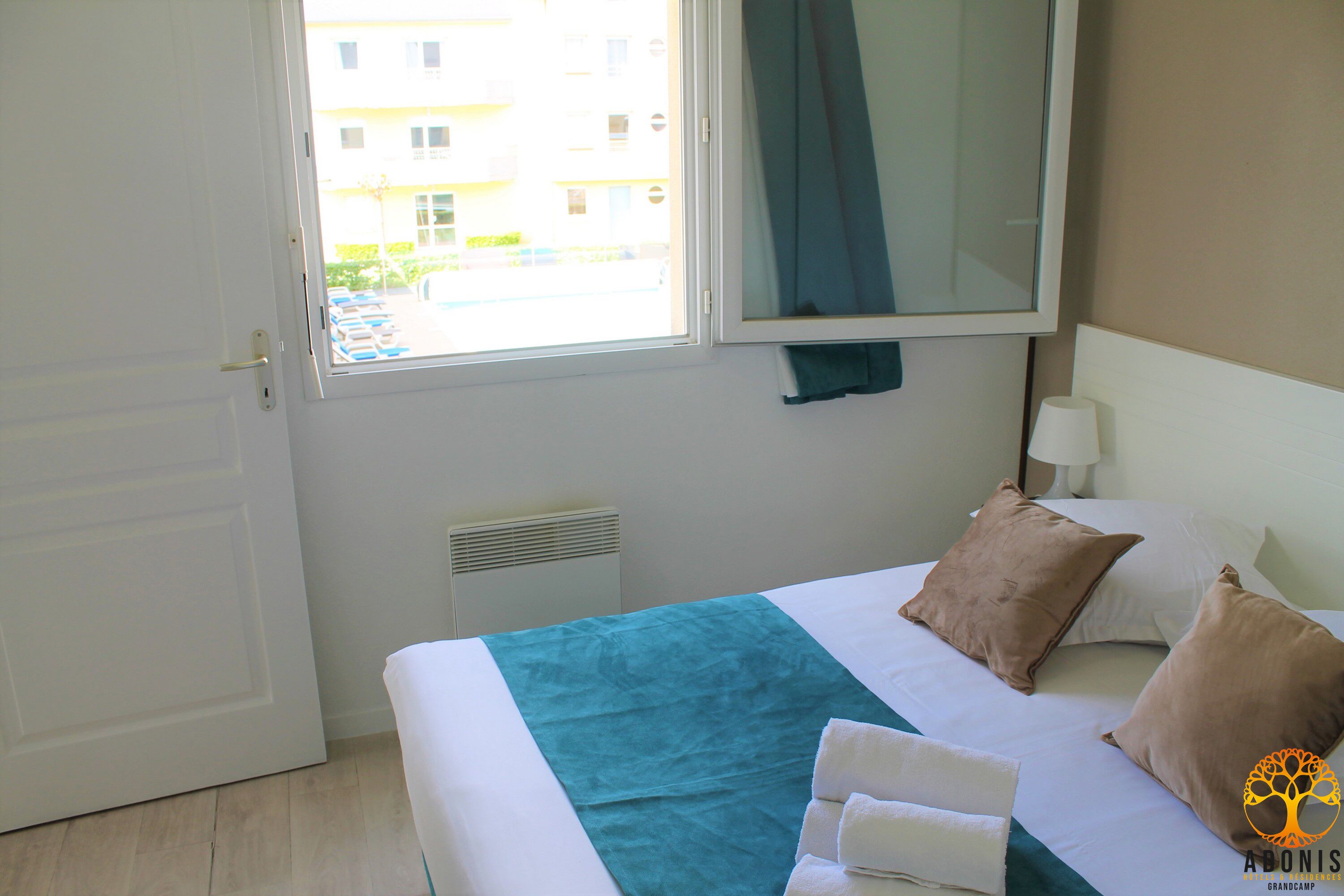 A hotel room with a bed, a window, a wall-mounted TV, and a visible outdoor view.