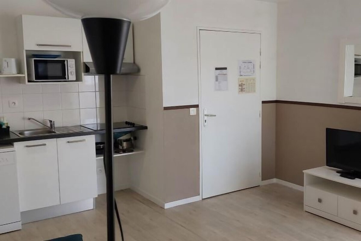 Cocina compacta con microondas, estufa y lavaplatos. Se observa una puerta con un calendario y un mueble pequeño con un televisor.
