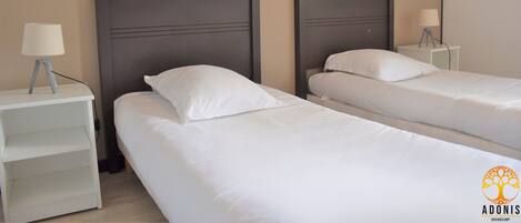 A hotel room with two single beds, each with a headboard and a bedside table with a lamp.