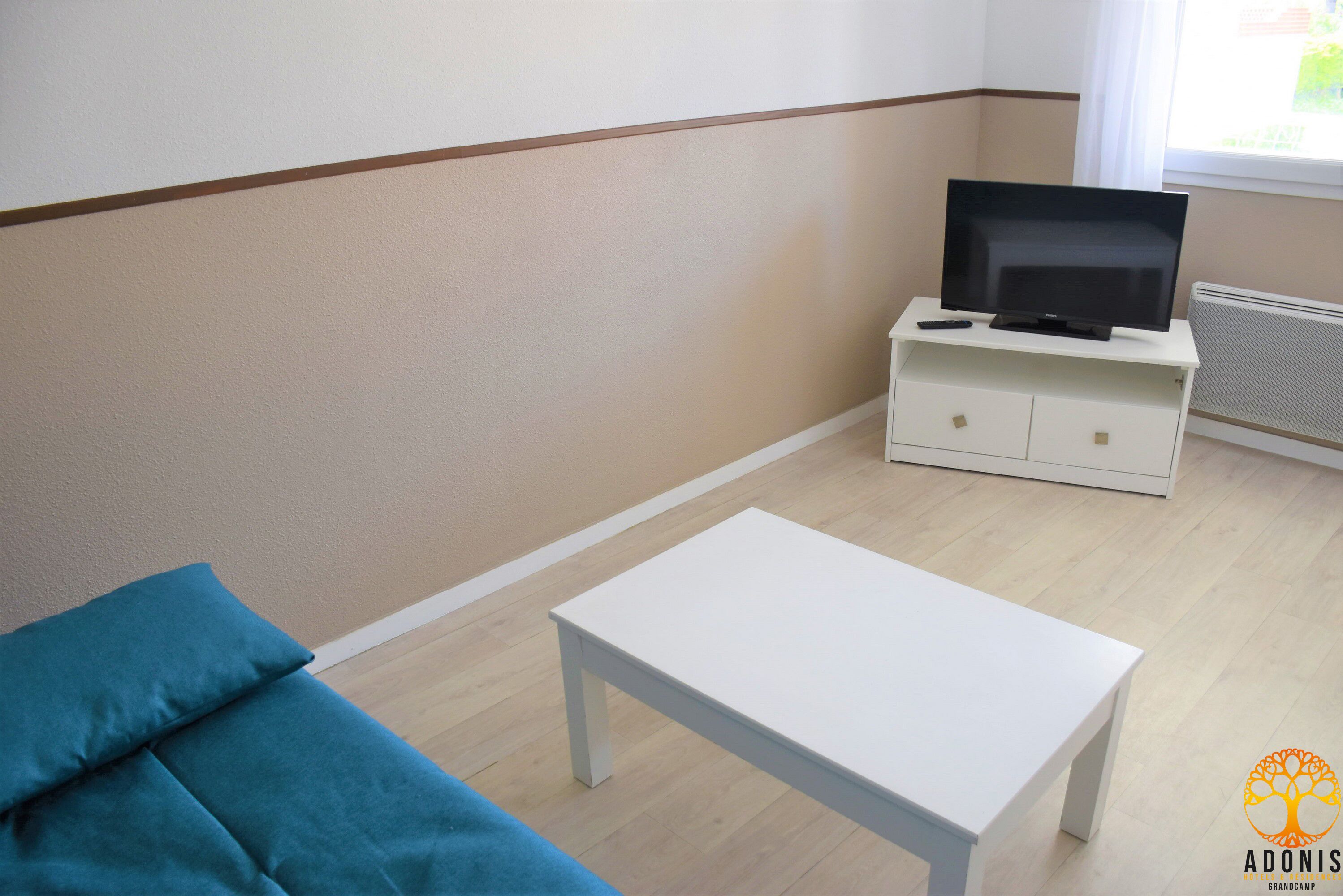 Een kamer met een witte tafel, een blauwe bank en een televisie op een witte kast.