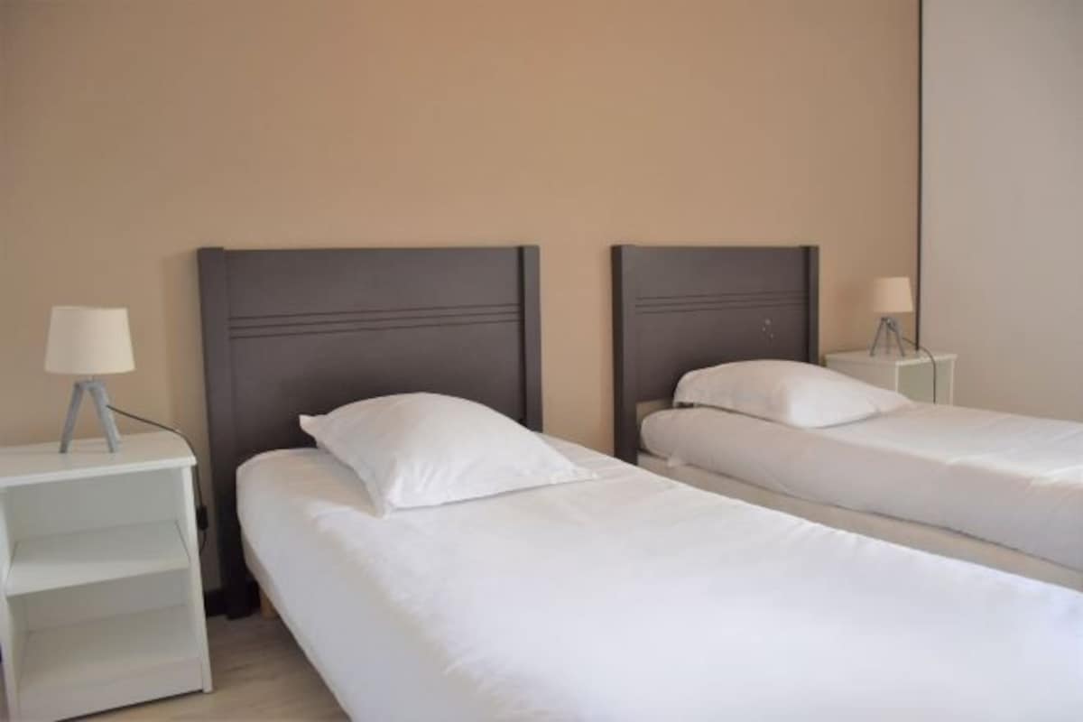 Dos camas individuales con cabeceras, ropa de cama blanca y mesitas de noche con lámparas.