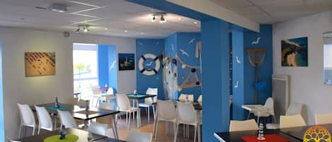 A dining area with tables and chairs, a blue accent wall, and nautical decorations.