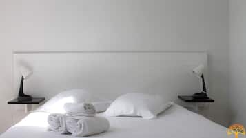 Un lit bien fait, avec du linge de lit blanc et des oreillers, deux tables de chevet avec des lampes, et une chambre au design épuré et minimaliste.