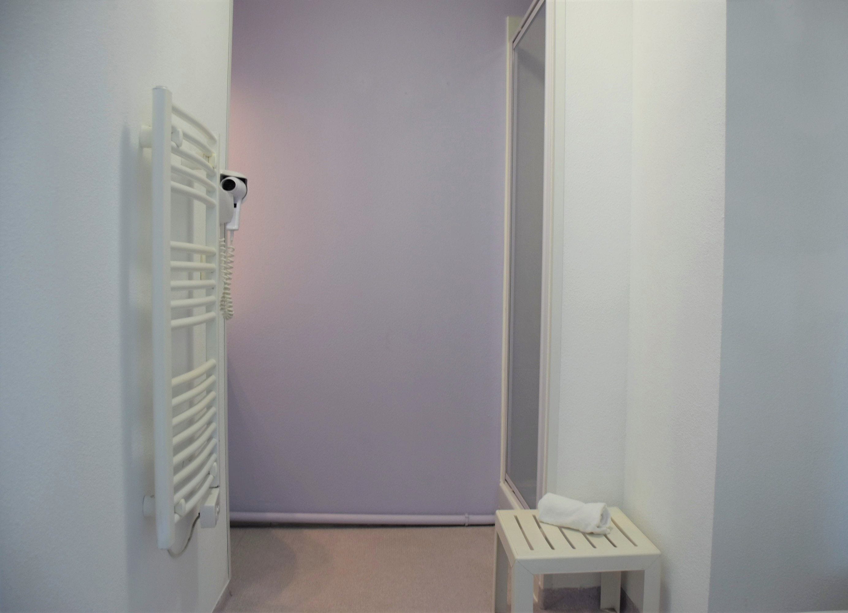 Un pasillo estrecho con un radiador, un taburete blanco pequeño y una puerta que da a otra habitación.