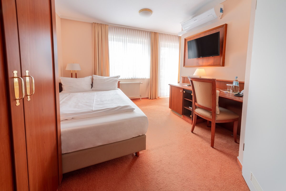 Een hotelkamer met een bed, een bureau, een stoel, een televisie en een radiator.