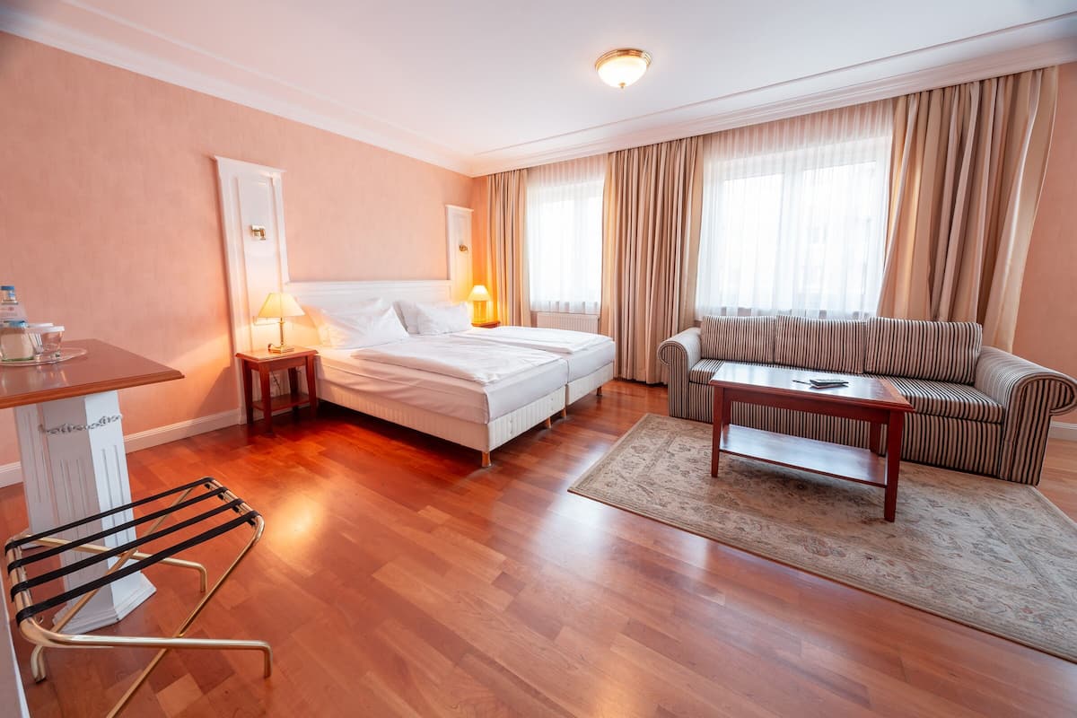 Een hotelkamer met een bed, een slaapbank, een tafel, een lamp, een radiator en een droogrek.