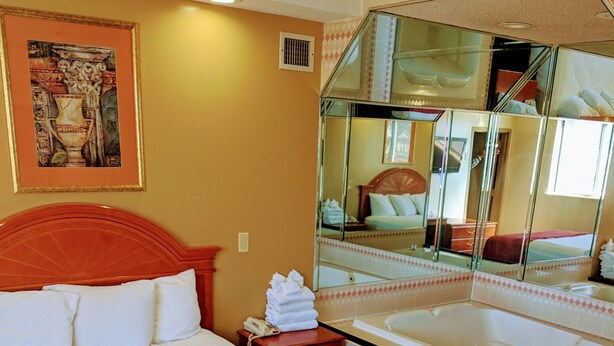 Une chambre d’hôtel avec un grand lit, une salle de bain avec une baignoire et un miroir qui reflète la pièce.