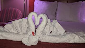 A hotel room with a bed, a lamp, and a heart-shaped towel arrangement on the bed.