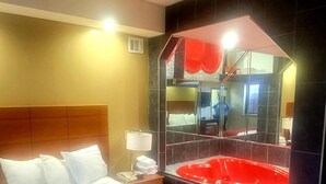 Une chambre d’hôtel avec un grand lit, une baignoire rouge et un grand miroir.