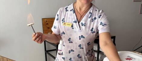 Una persona recibiendo un tratamiento en la espalda en una habitación con un reloj en la pared, un estante de madera y una etiqueta con el nombre del terapeuta en su uniforme.