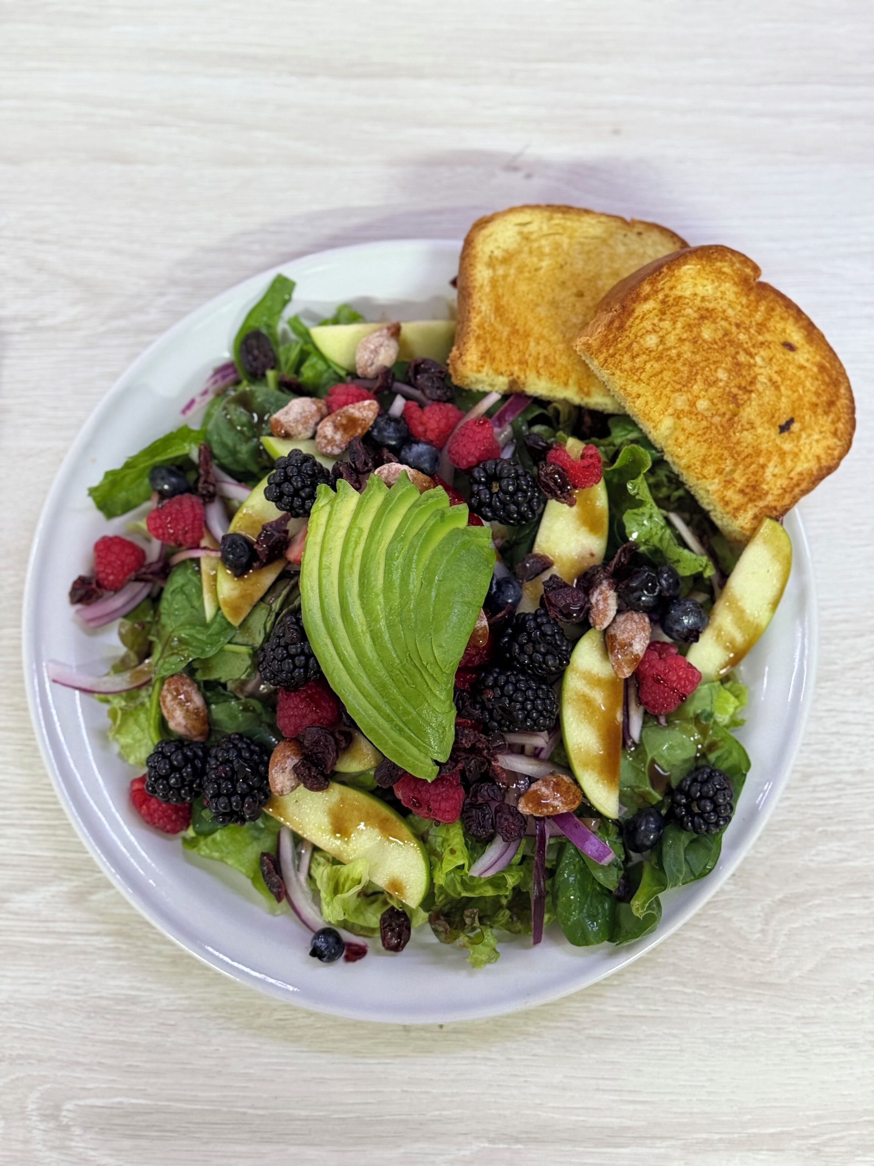 A salad with various fruits and nuts, accompanied by two toasted bread slices.