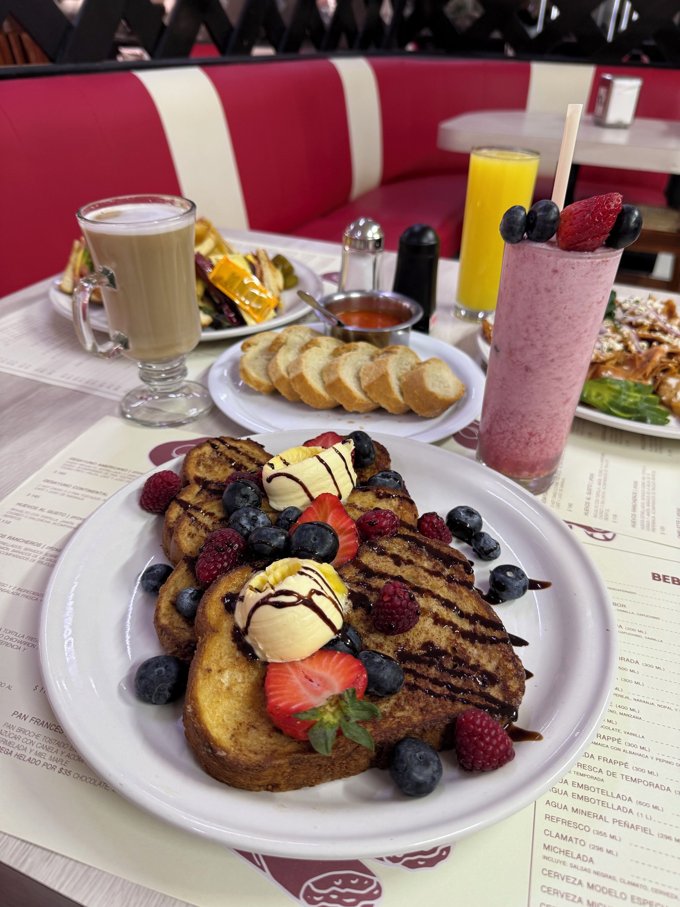 Mesa posta para o café da manhã, com panquecas, frutas e uma bebida.