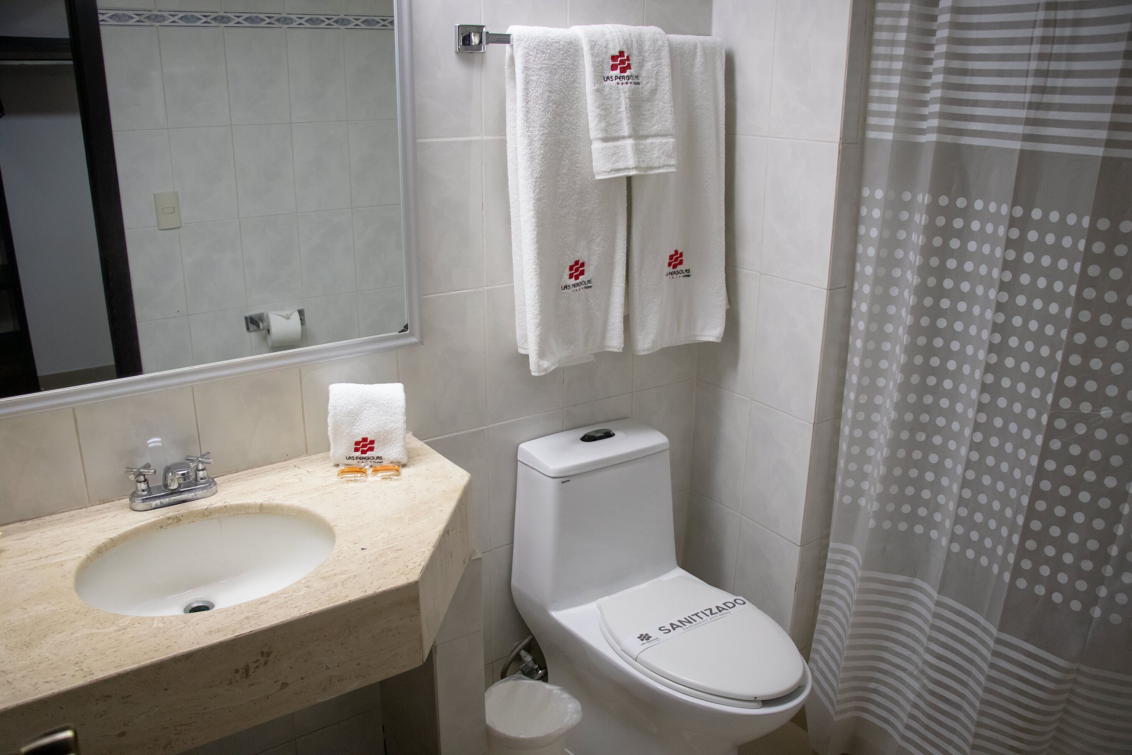 A bathroom with a sink, toilet, and a mirror. There are two towels hanging on the wall, and a shower curtain with a polka dot pattern.