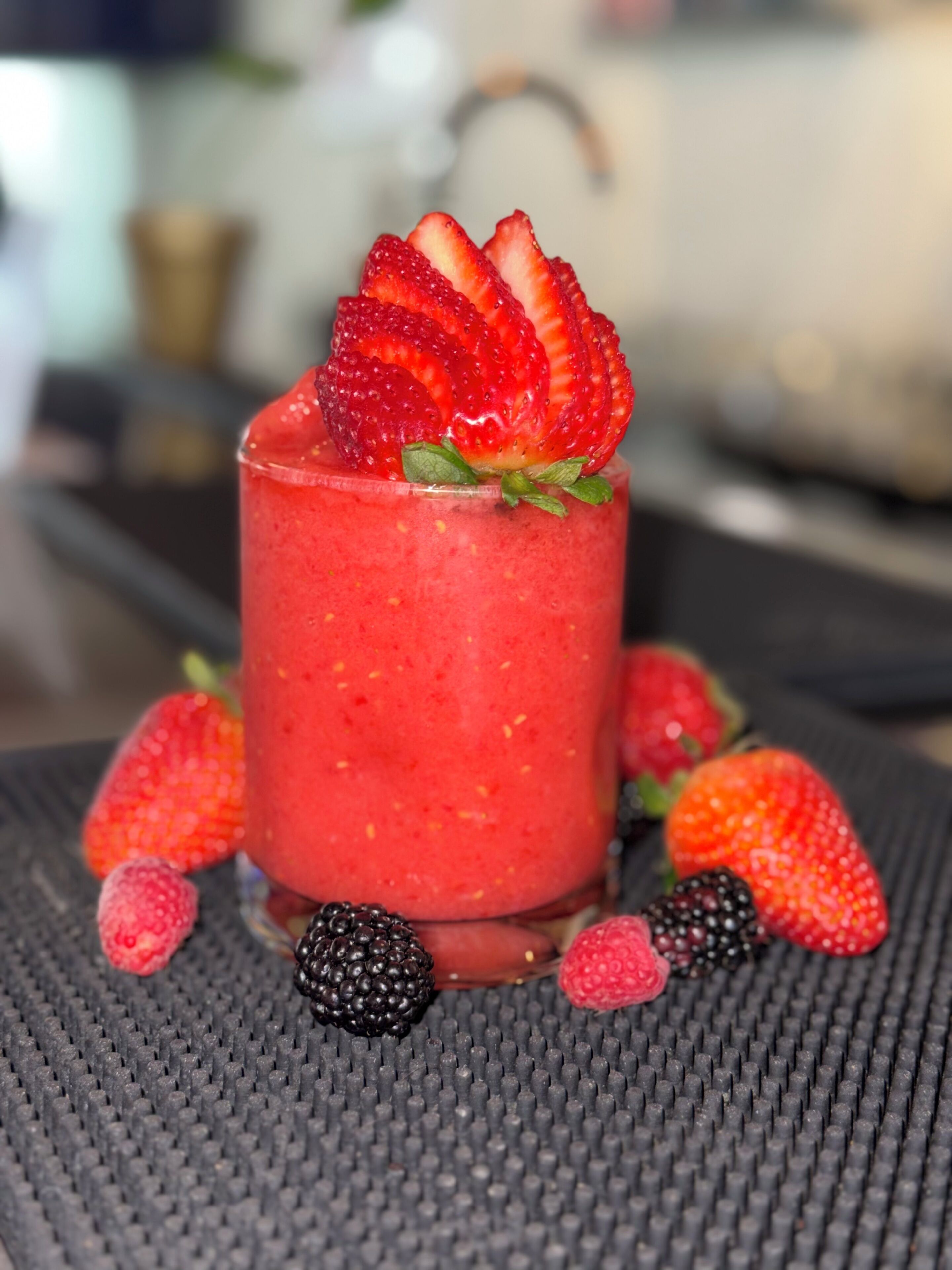Una bebida con fresas y frambuesas sobre una superficie texturizada.