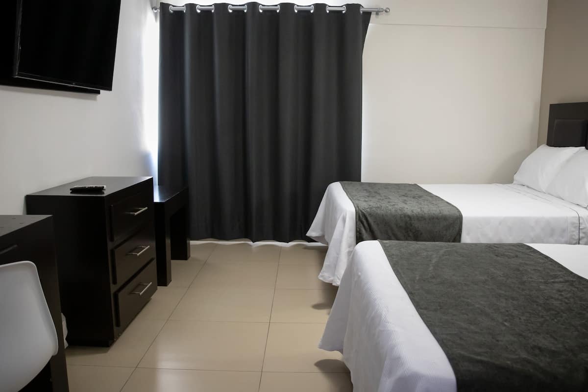 Una habitación de hotel con dos camas, un escritorio, una silla, un televisor y una cortina.