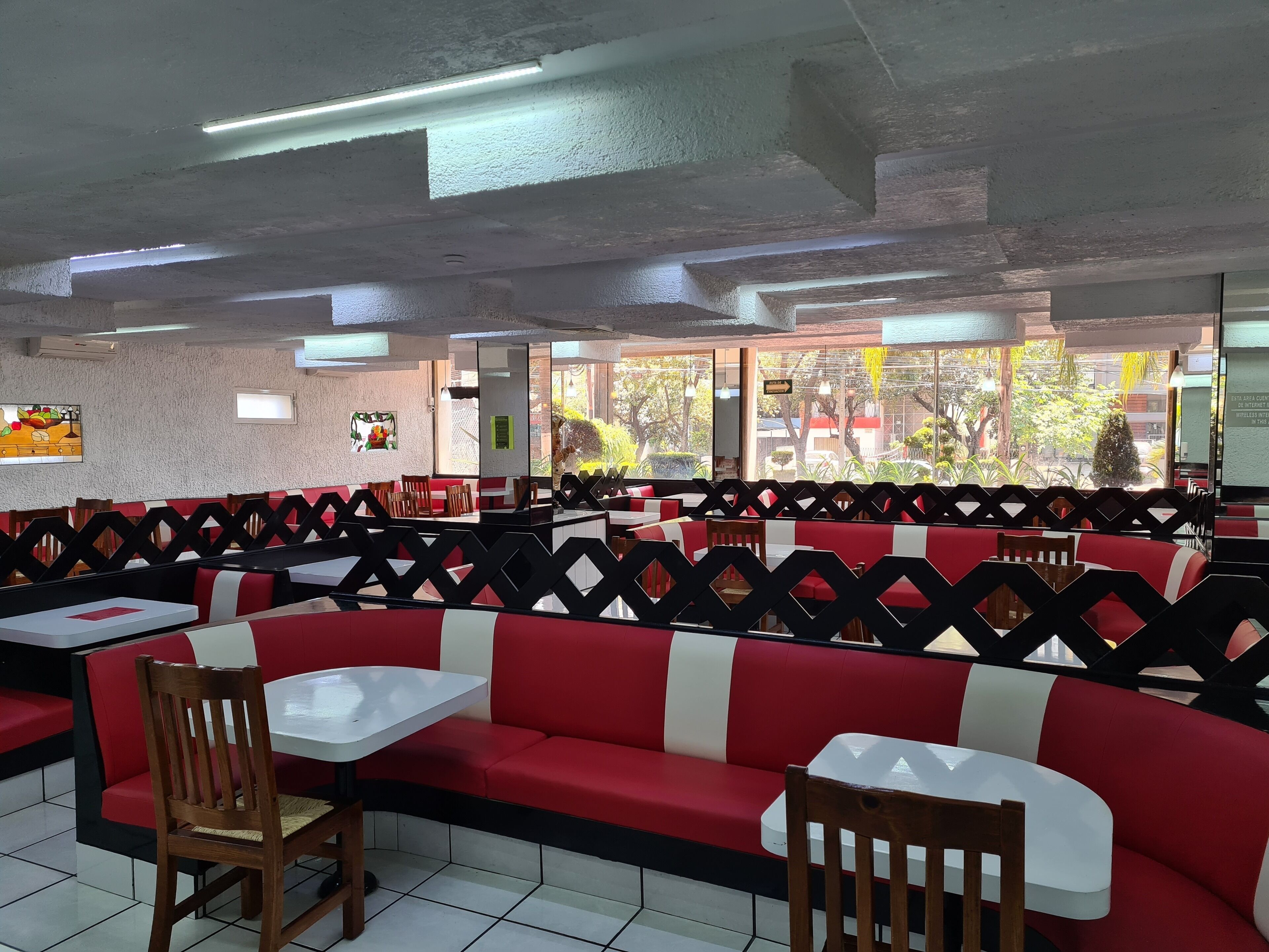 Un restaurant avec des banquettes rouges et blanches, des tables blanches et un sol carrelé.