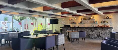 Zona de bar con barra, estanterías llenas de botellas y un área de estar con mesas y sillas.