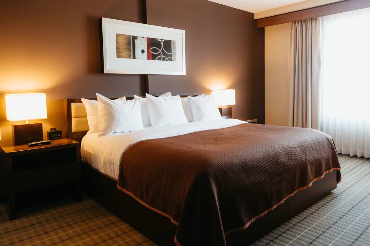 A hotel room with a large bed, two bedside tables with lamps, a framed artwork above the bed, and a window with curtains.