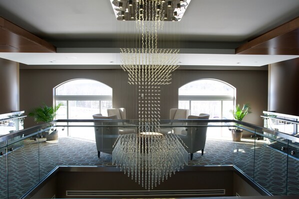 A modern lobby with a central chandelier, glass railings, seating areas, and large windows. - Casino New Brunswick (Moncton)