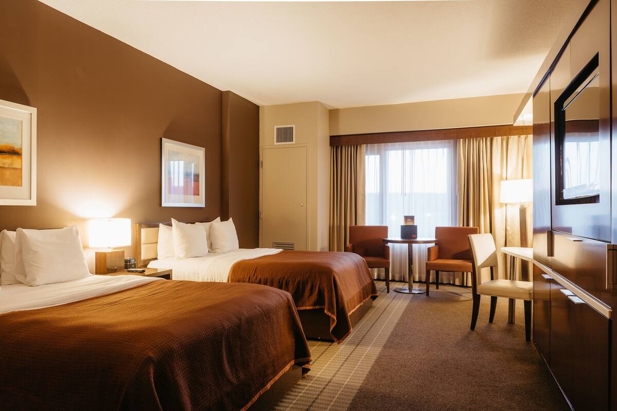 A hotel room with two beds, a desk, a chair, a TV, and a window with curtains.