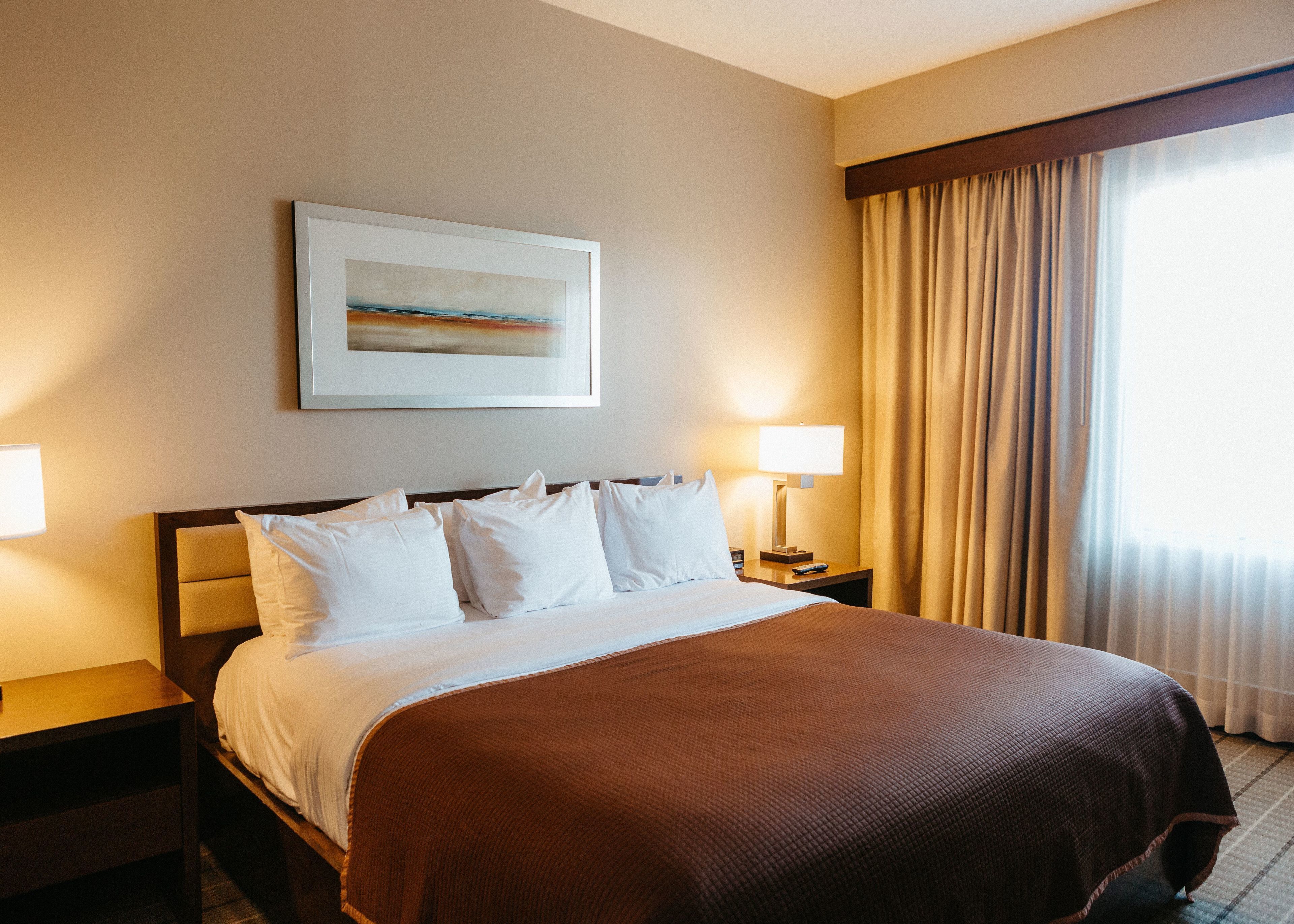 A hotel room with a large bed, two bedside tables, a framed picture on the wall, and a window with curtains.