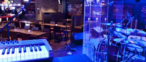 A music studio with a keyboard and drum set, tables, chairs, and a brick wall.