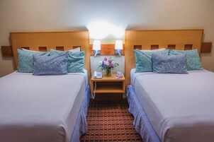 Habitación de hotel con dos camas, cada una con cabecero de madera, una mesita de noche entre ellas y una pequeña mesa con un teléfono y un florero.