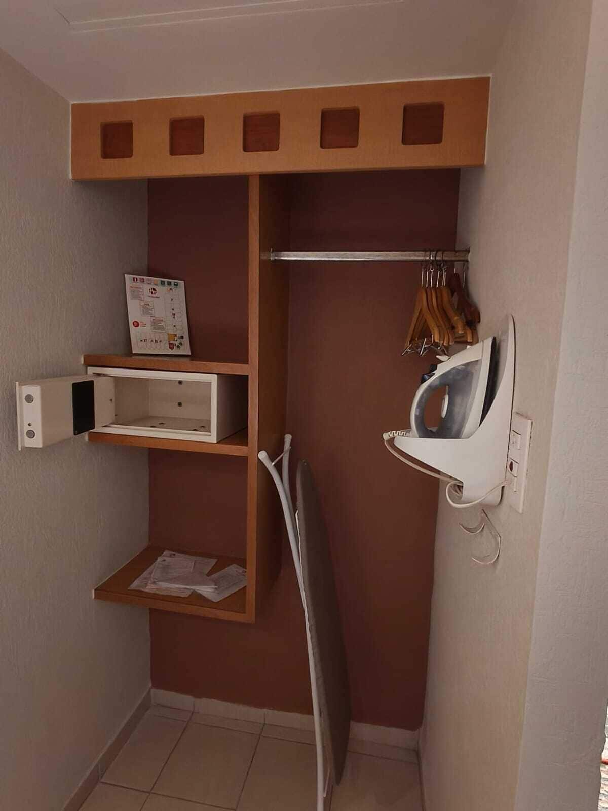 A compact utility room with a wooden shelf unit, a hanging rack for clothes, and a wall-mounted ironing board.