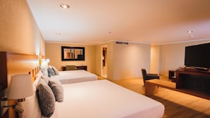 A hotel room with two beds, a desk, a chair, a television, and a bench. - Hotel Mirabel (Querétaro)