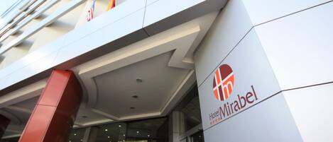 The exterior of a hotel with a modern design, featuring a prominent logo and a glass entrance.