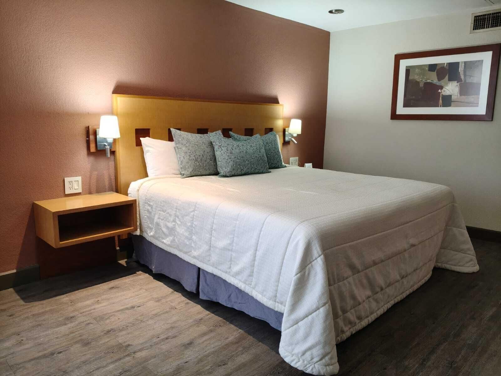 A hotel room with a large bed, two bedside tables with lamps, a wooden headboard, and a framed picture on the wall.