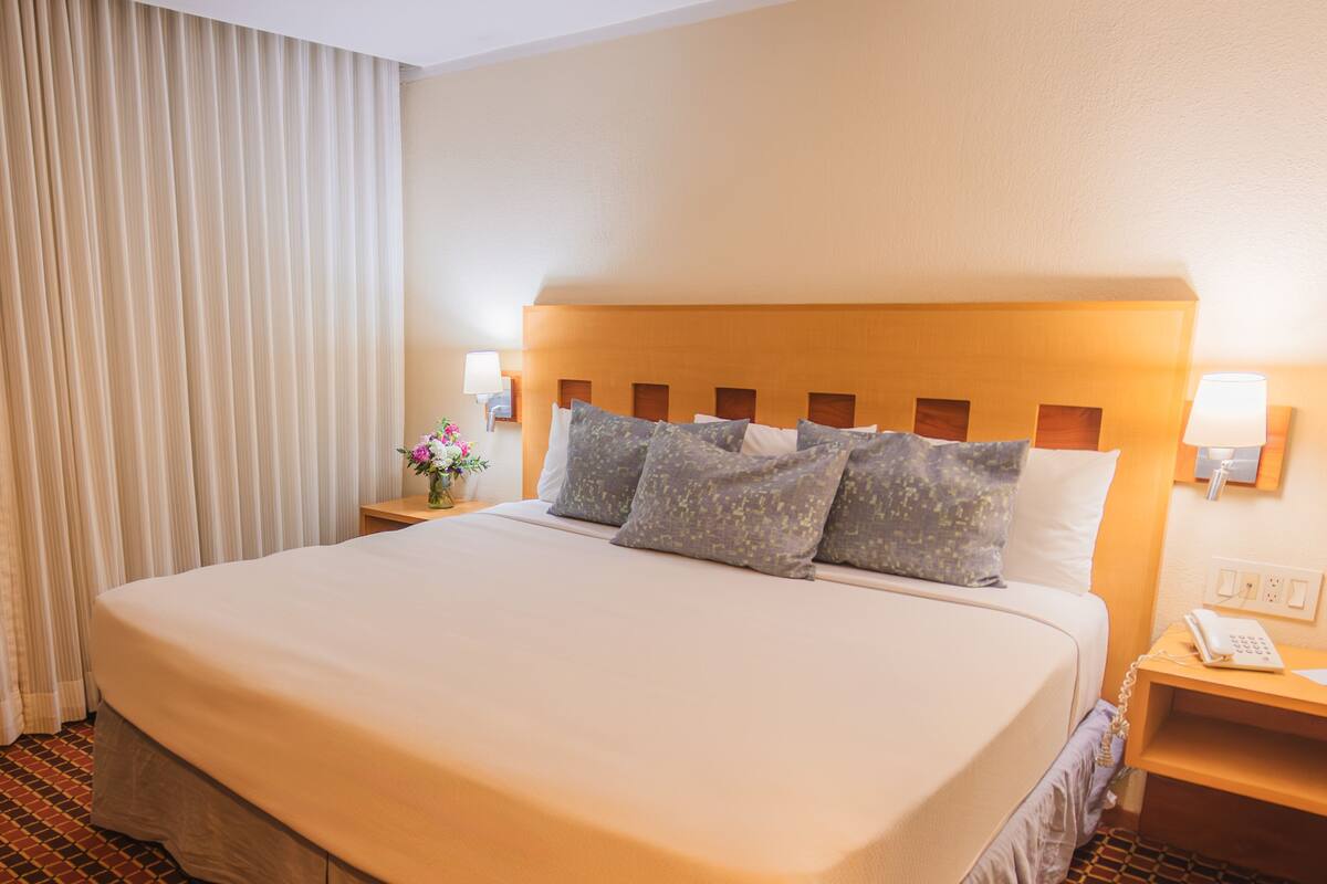 A hotel room with a large bed, two bedside tables, a nightstand, and a lamp.