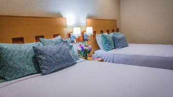 A hotel room with two beds, each with a headboard, pillows, a nightstand with a lamp, and a vase with flowers.