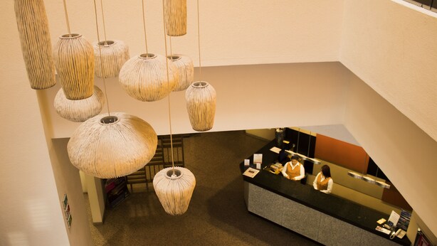 A hotel reception area with a counter, several hanging light fixtures, and a staircase. - Hotel Mirabel (Querétaro)
