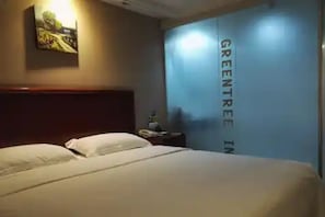 A hotel room with a bed, a nightstand, a painting on the wall, and a wall with the text "GREENTREE IN".