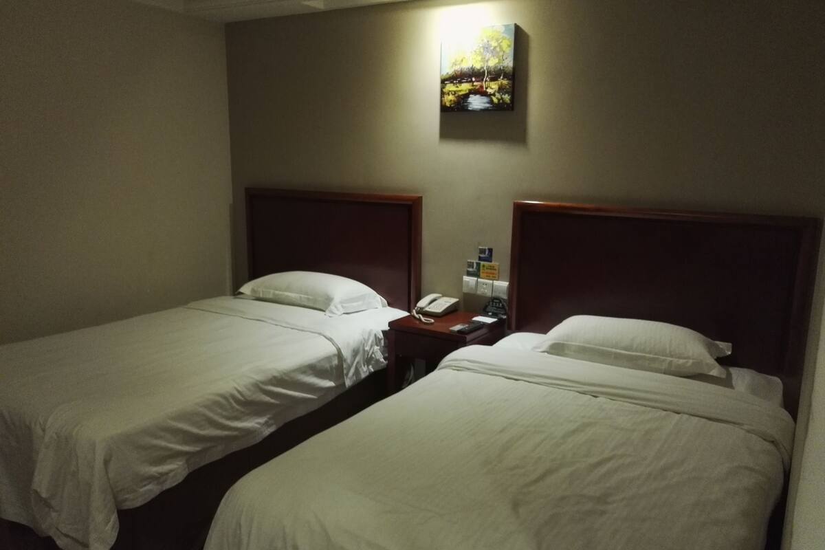 Une chambre d’hôtel avec deux lits simples, une table de chevet avec un téléphone et une télécommande, et un tableau au mur.
