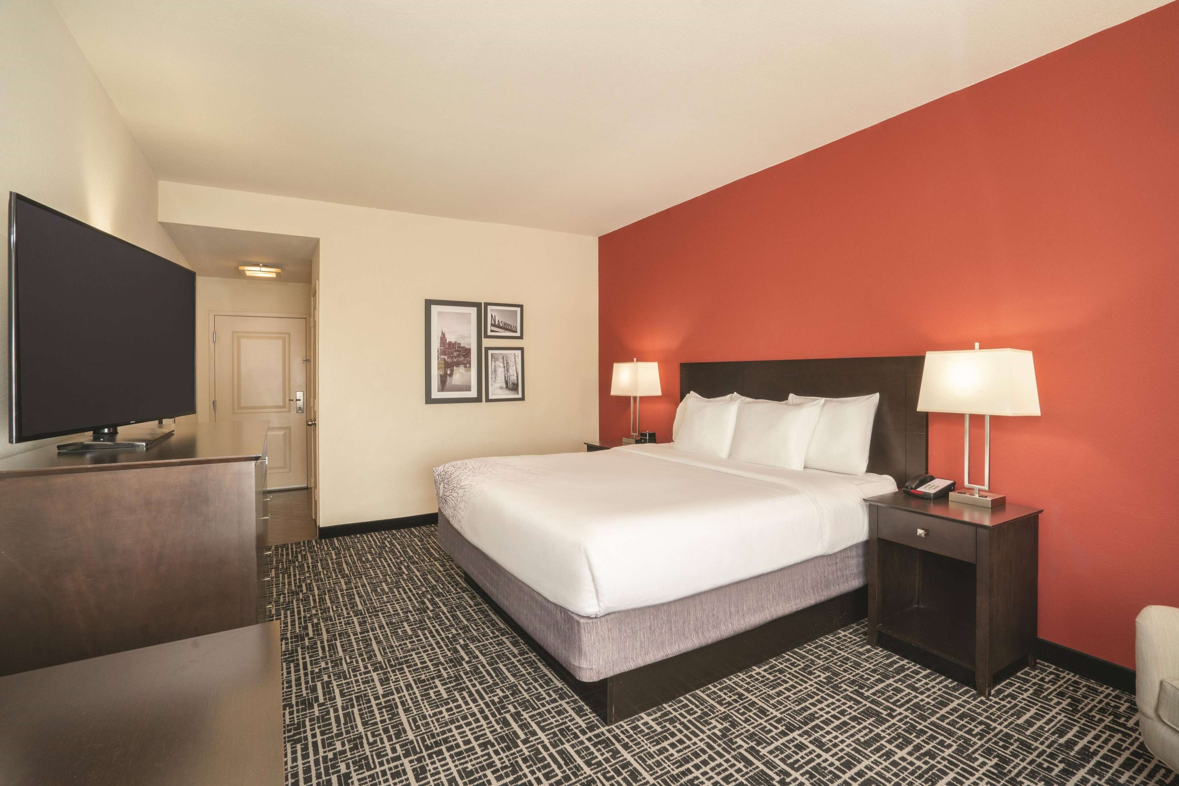 A hotel room with a large bed, two bedside tables with lamps, a flat-screen TV, and a patterned carpet.