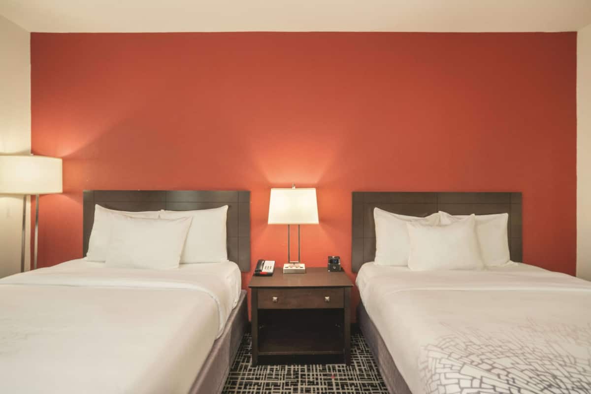 Ein Hotelzimmer mit zwei Betten, einem Nachttisch mit Lampe und einer roten Akzentwand.
