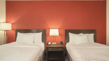 A hotel room with two beds, a nightstand with a lamp, and a red accent wall.