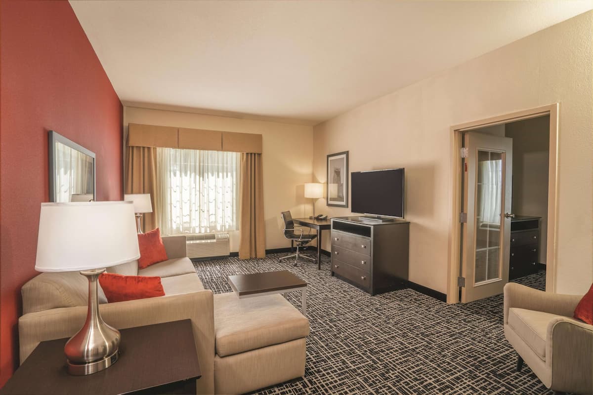 Ein Hotelzimmer mit Sofa, Sesseln, Schreibtisch, Fernseher und Minibar.