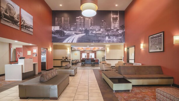 A hotel lobby with a reception desk, seating areas, and a large cityscape mural on the wall. - La Quinta Inn & Suites by Wyndham Smyrna TN - Nashville (Smyrna)
