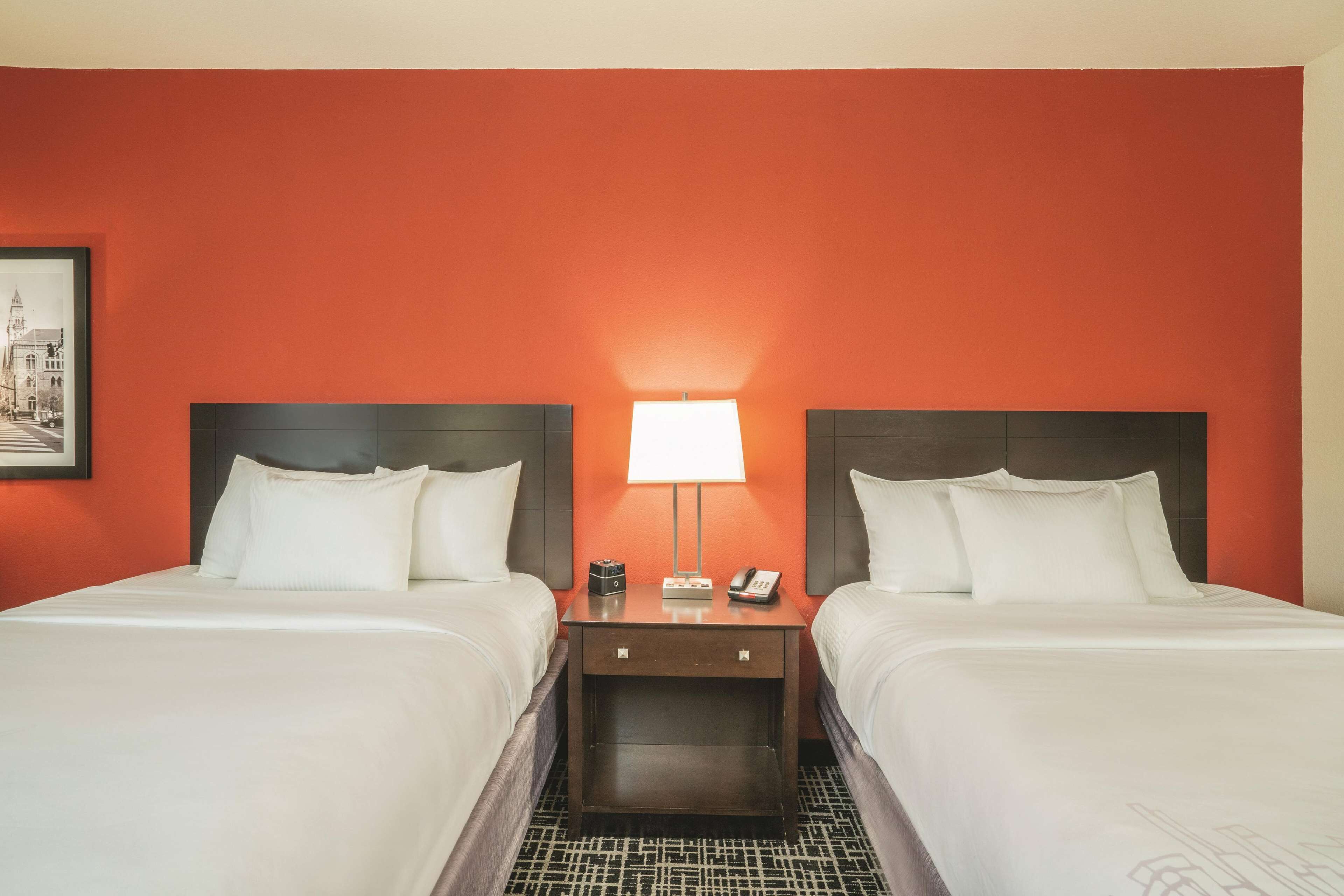 Habitación de hotel con dos camas, una mesita de noche con lámpara y un cuadro enmarcado en la pared.