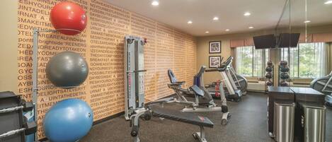 A gym with exercise equipment, a wall with motivational quotes, and a window with a view of trees.