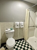 Un baño con inodoro, ducha y piso de cuadros.