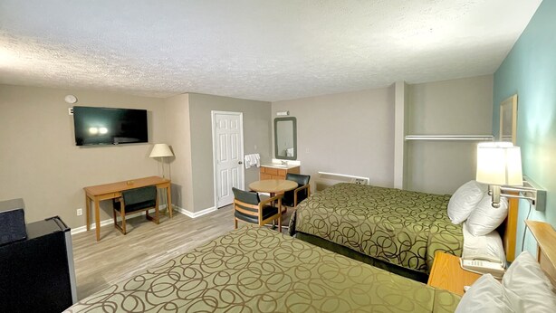 Habitación de hotel con dos camas, un escritorio, una silla, un televisor, un espejo y una lámpara.