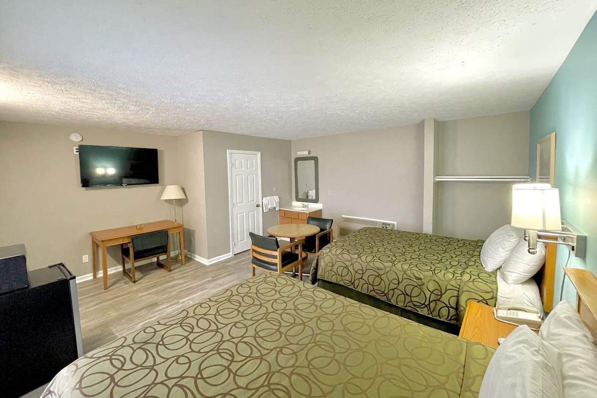 A hotel room with two beds, a desk, a chair, a TV, a mirror, and a lamp.