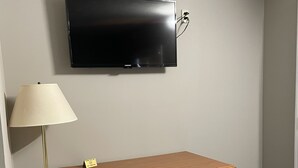 Una habitación con un escritorio de madera, una butaca tapizada en verde, una lámpara de pie y un televisor de pantalla plana montado en la pared.
