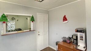 Una habitación de hotel con un aparador de madera, una cafetera, un cesto de basura pequeño y una puerta.